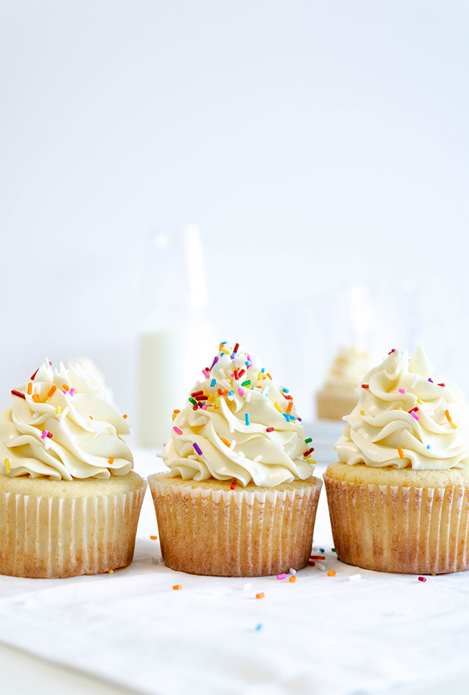three confetti cupcakes on a table with sprinkles